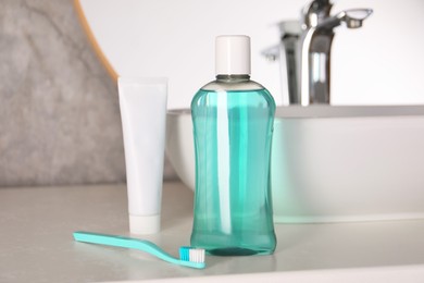 Bottle of mouthwash, toothpaste and toothbrush on light countertop in bathroom