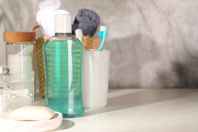 Photo of Bottle of mouthwash, toothbrushes and soap on light table in bathroom, space for text