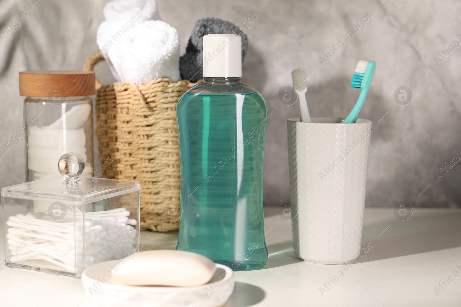 Photo of Bottle of mouthwash, toothbrushes and soap on light table in bathroom