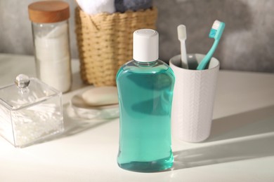 Bottle of mouthwash and toothbrushes on light table in bathroom