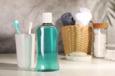 Bottle of mouthwash and toothbrushes on light table in bathroom