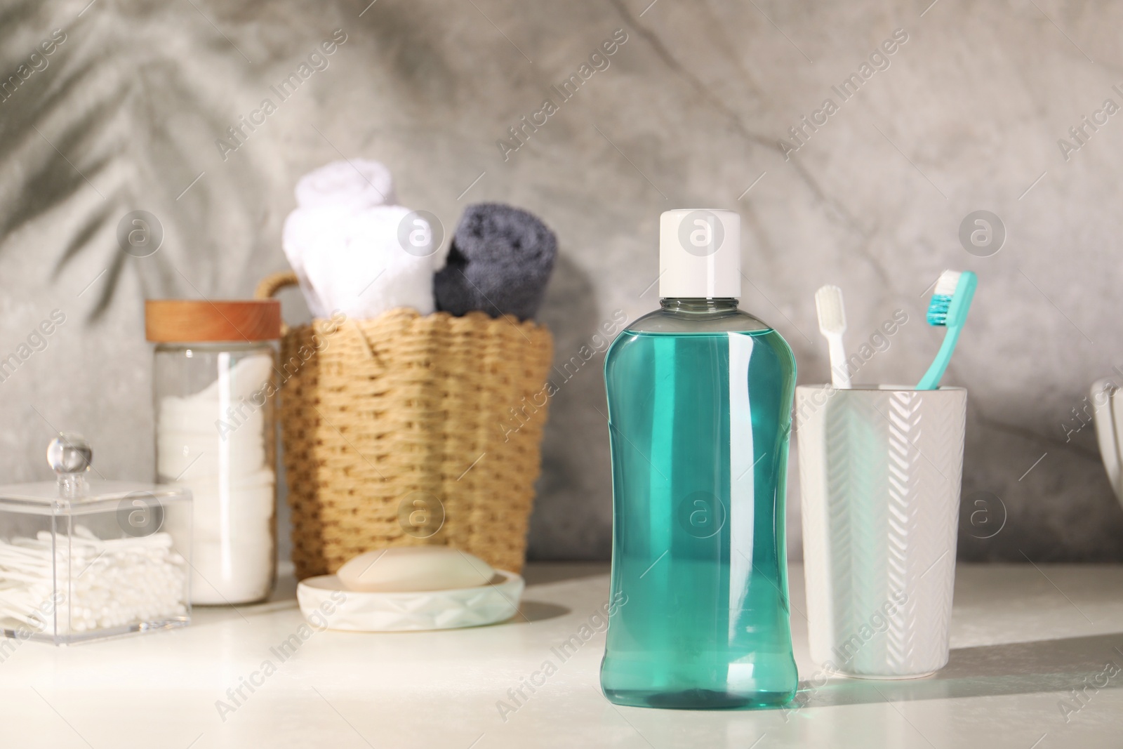 Photo of Bottle of mouthwash and toothbrushes on light table in bathroom