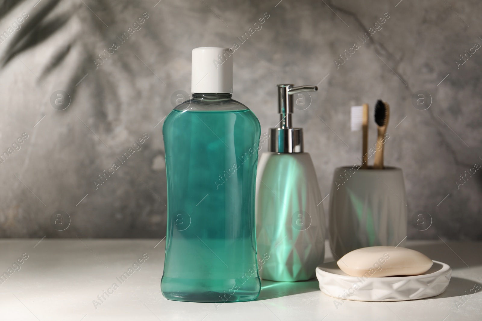 Photo of Bottle of mouthwash, toothbrushes and soap on light table in bathroom