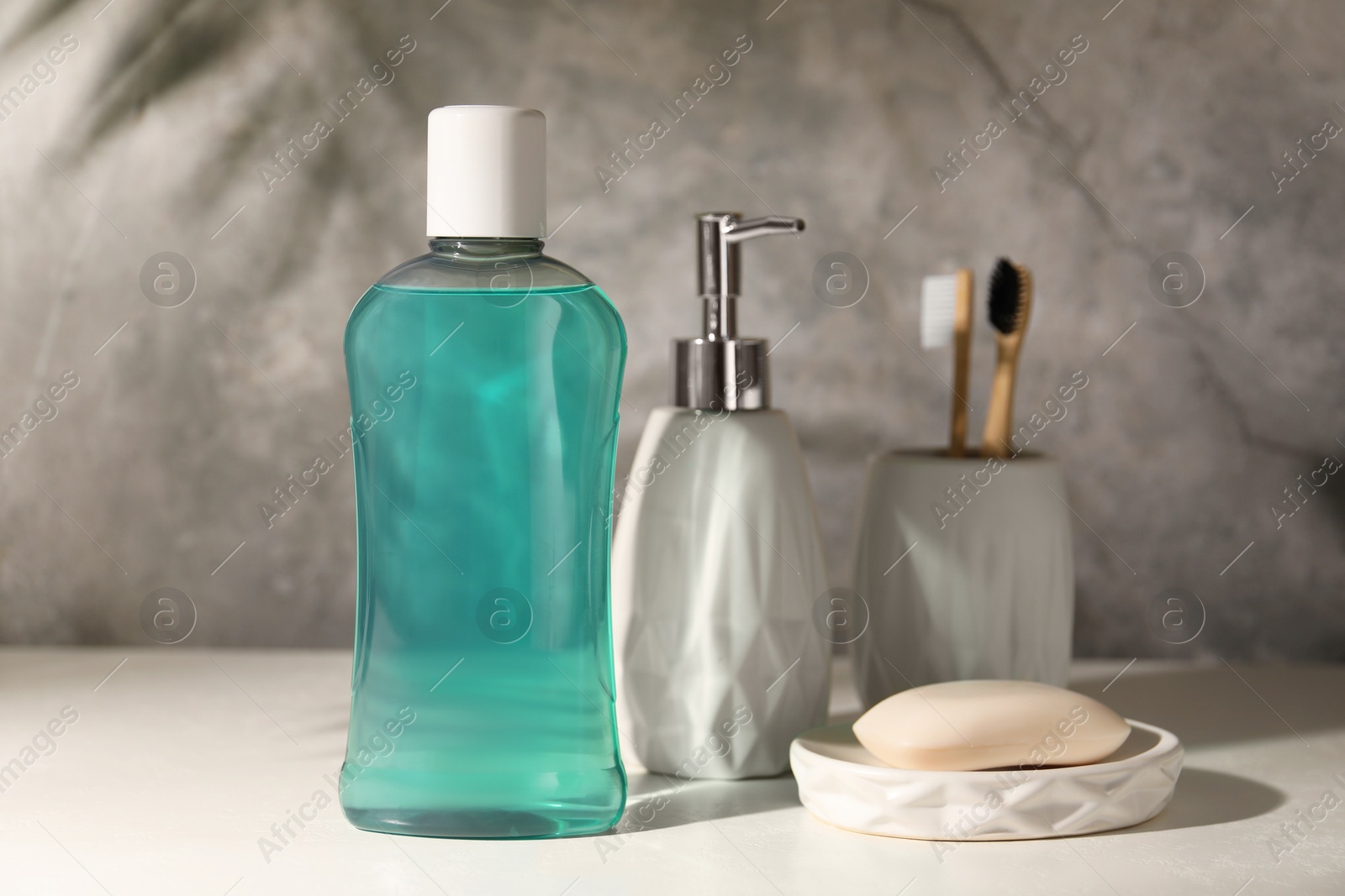 Photo of Bottle of mouthwash, toothbrushes and soap on light table in bathroom