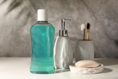 Bottle of mouthwash, toothbrushes and soap on light table in bathroom