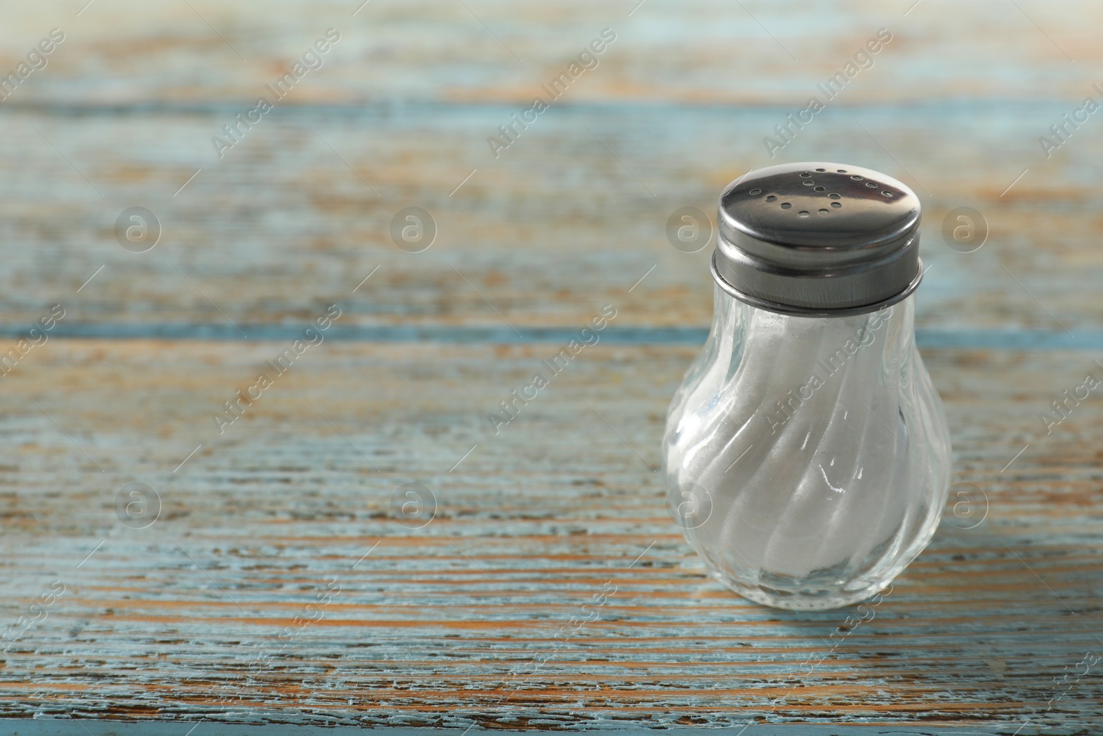 Photo of Salt shaker on light blue wooden table, closeup. Space for text