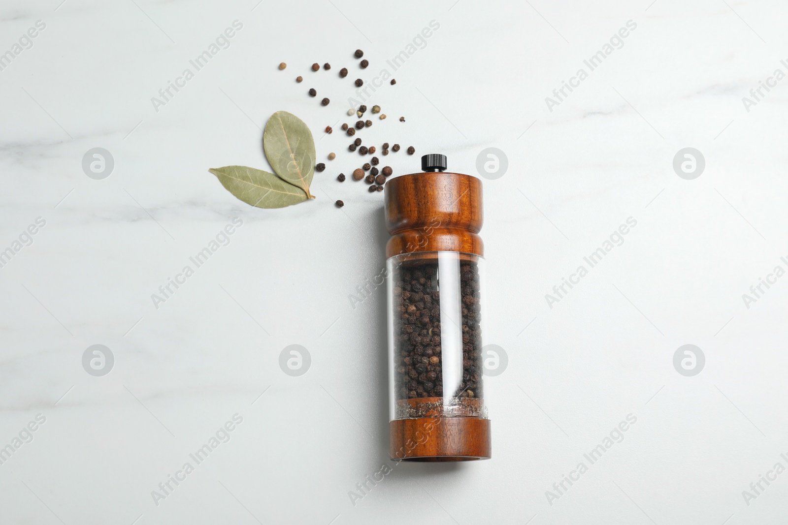 Photo of Pepper shaker and bay leaves on white marble table, flat lay