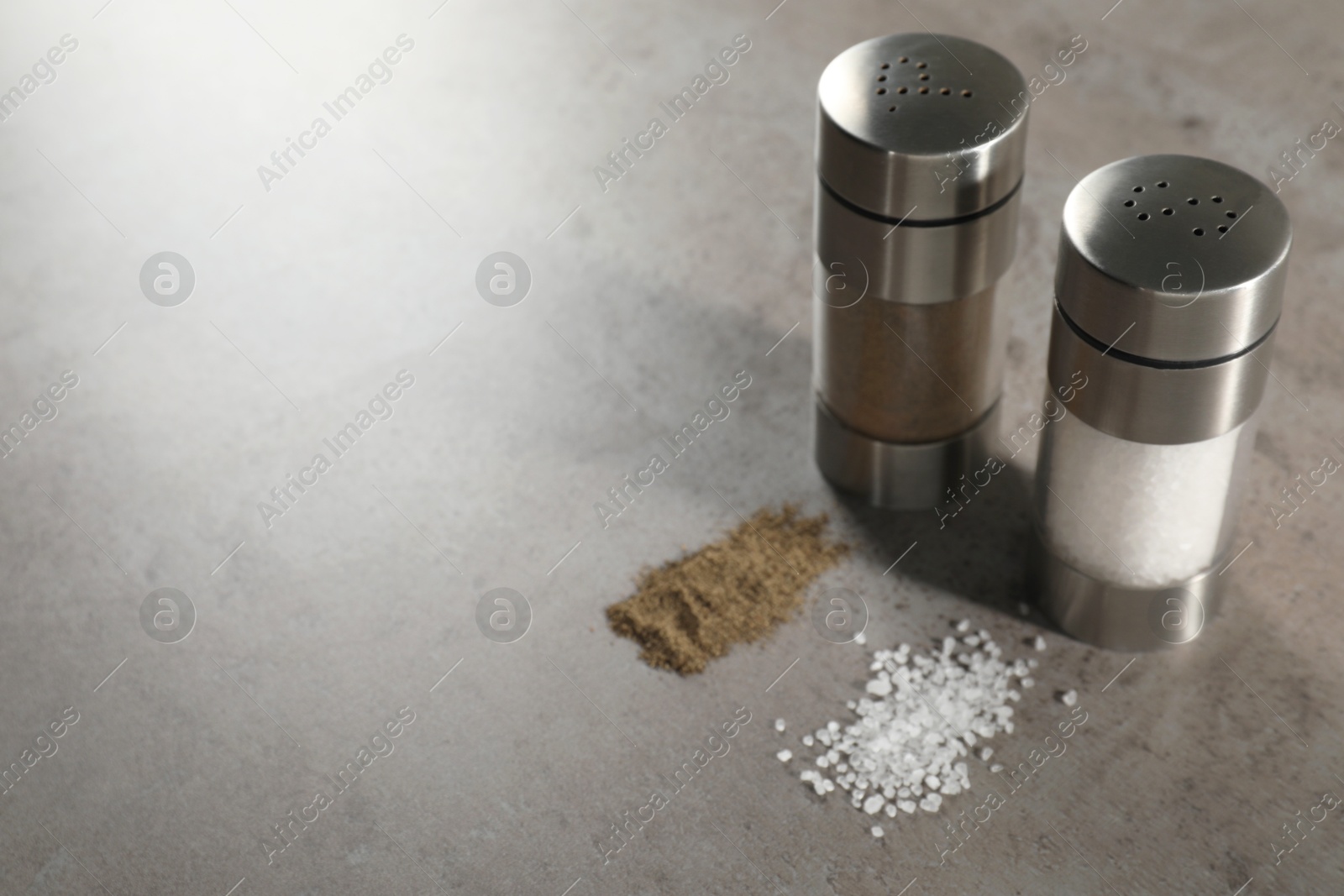 Photo of Salt and pepper shakers on grey textured table, closeup. Space for text