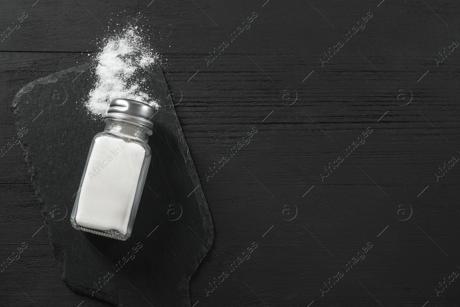 Photo of Salt shaker on black wooden table, top view. Space for text