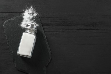 Salt shaker on black wooden table, top view. Space for text