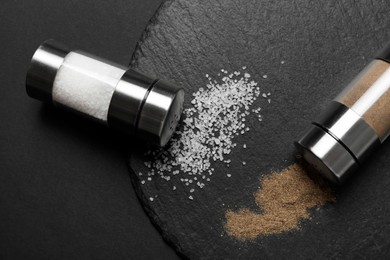 Photo of Salt and pepper shakers on dark table, flat lay