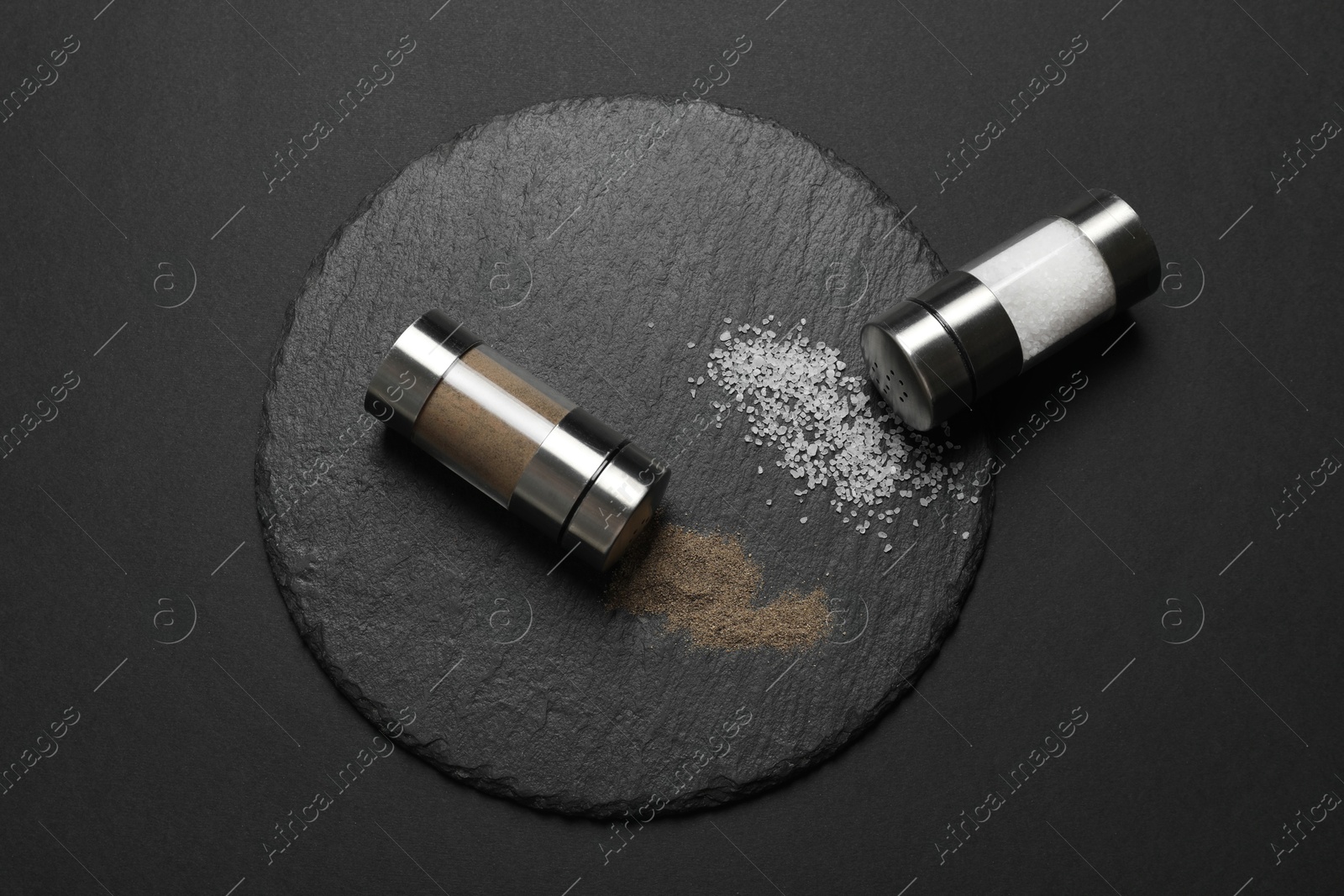 Photo of Salt and pepper shakers on dark table, flat lay