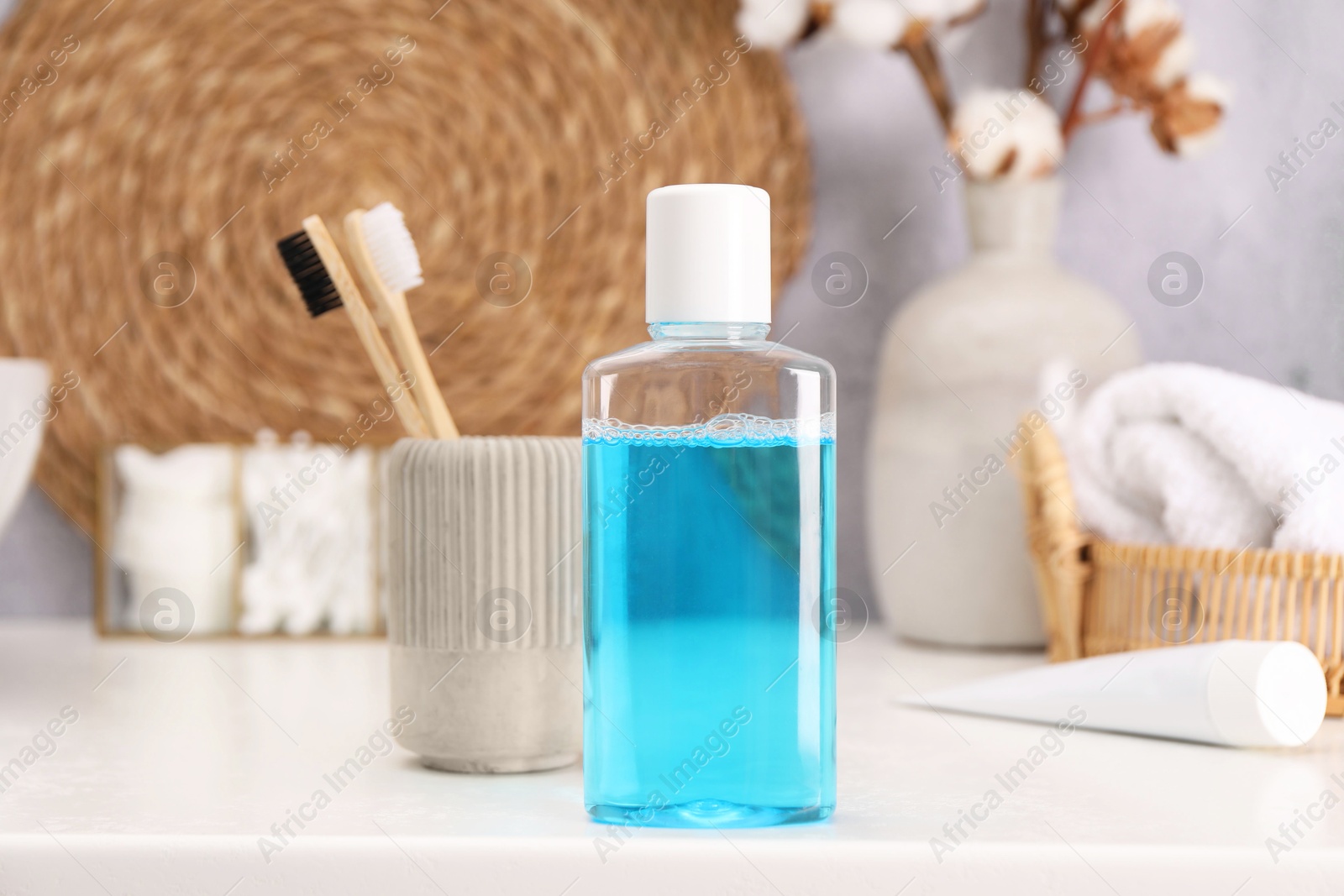 Photo of Bottle of mouthwash and toothbrushes on white table in bathroom