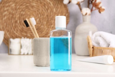 Photo of Bottle of mouthwash and toothbrushes on white table in bathroom