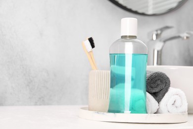 Bottle of mouthwash, toothbrushes and towels on white table in bathroom, space for text