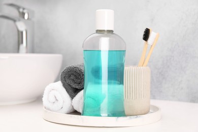 Photo of Bottle of mouthwash, toothbrushes and towels on white table in bathroom