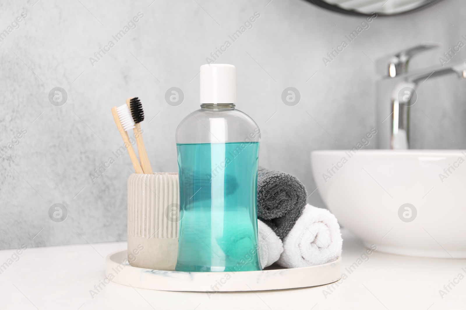 Photo of Bottle of mouthwash, toothbrushes and towels on white table in bathroom