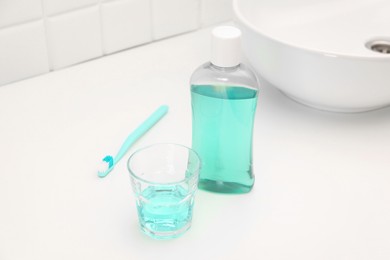 Photo of Bottle of mouthwash, toothbrush and glass on white table in bathroom