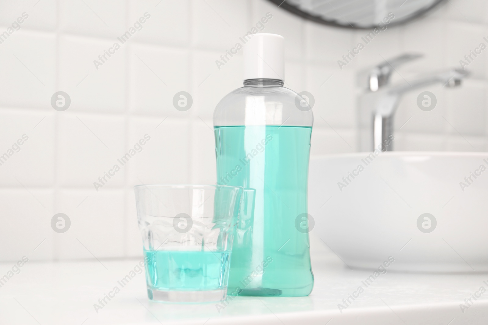 Photo of Bottle of mouthwash and glass on white table in bathroom