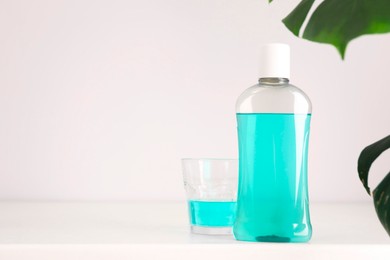 Bottle of mouthwash and glass on white table in bathroom, space for text