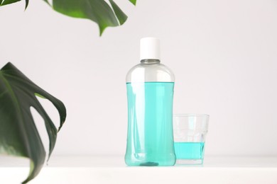 Photo of Bottle of mouthwash and glass on white table in bathroom