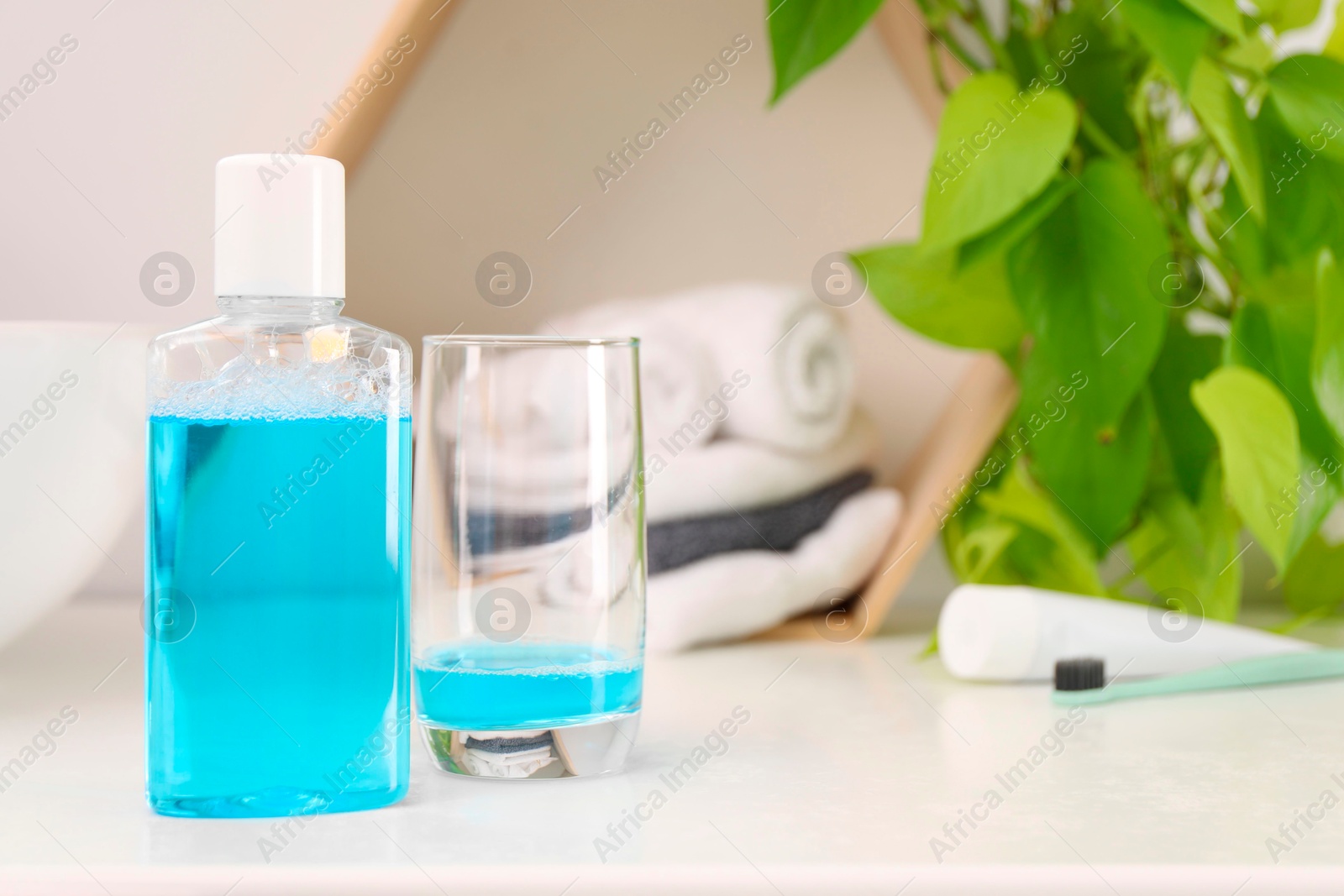 Photo of Bottle of mouthwash and glass on white table in bathroom, space for text