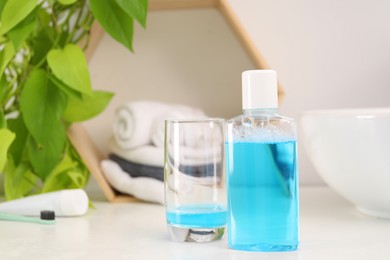 Photo of Bottle of mouthwash and glass on white table in bathroom