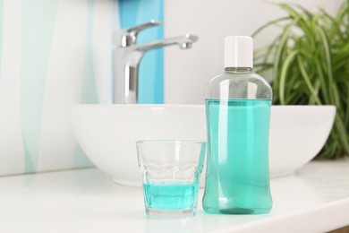 Photo of Bottle of mouthwash and glass on white table in bathroom