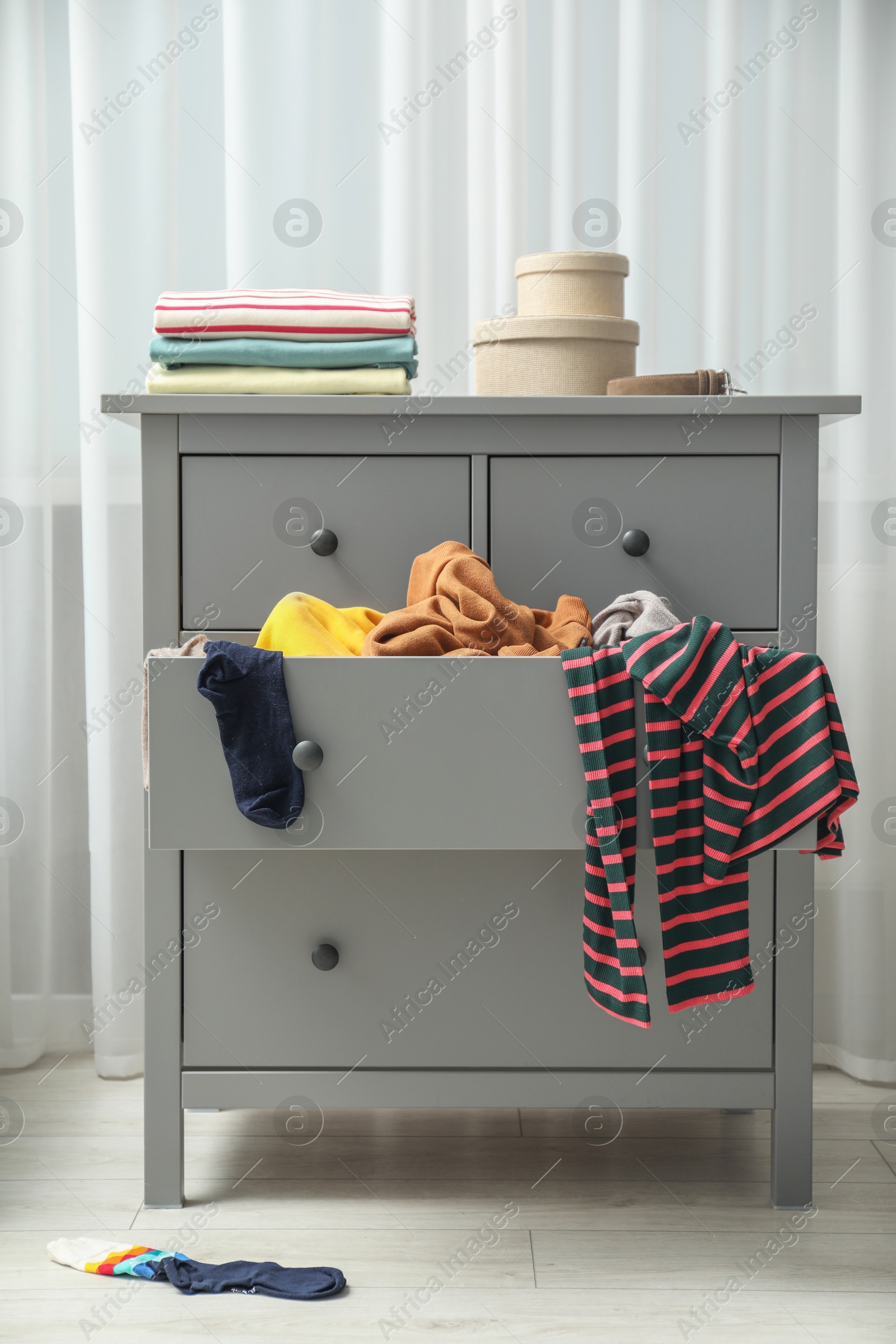 Photo of Cluttered chest of drawers indoors. Clothes in mess