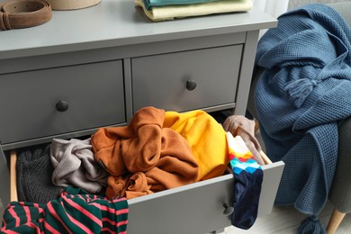 Cluttered chest of drawers indoors. Clothes in mess