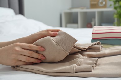 Woman folding clothes on bed indoors, closeup