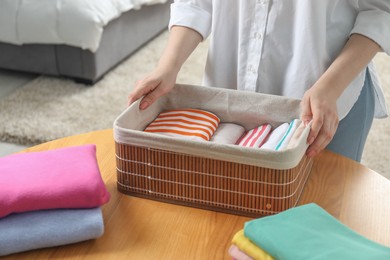 Woman holding basket with folded clothes at table indoors, closeup