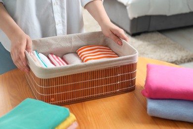 Photo of Woman holding basket with folded clothes at table indoors, closeup