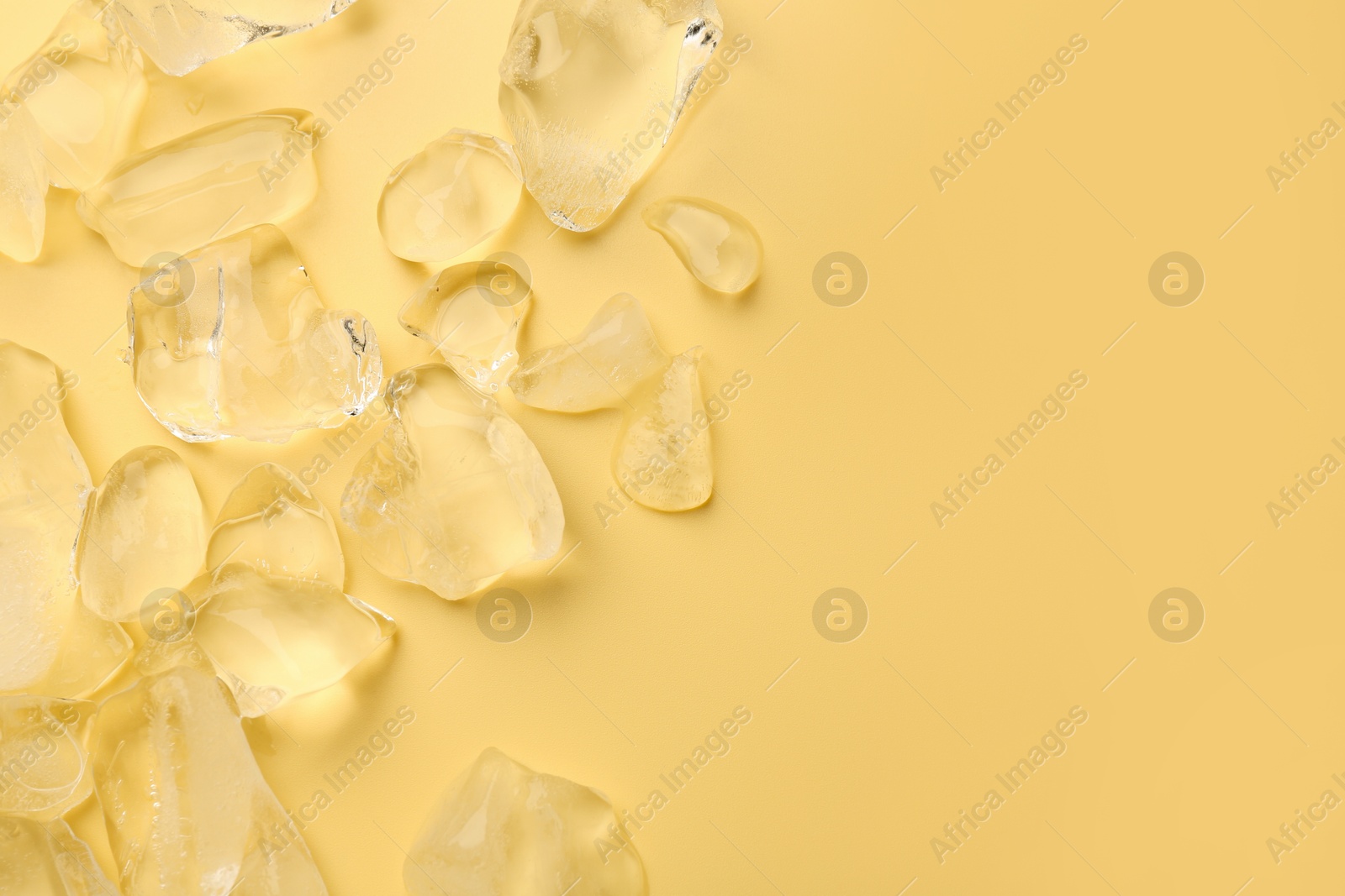 Photo of Pieces of crushed ice on yellow background, top view. Space for text