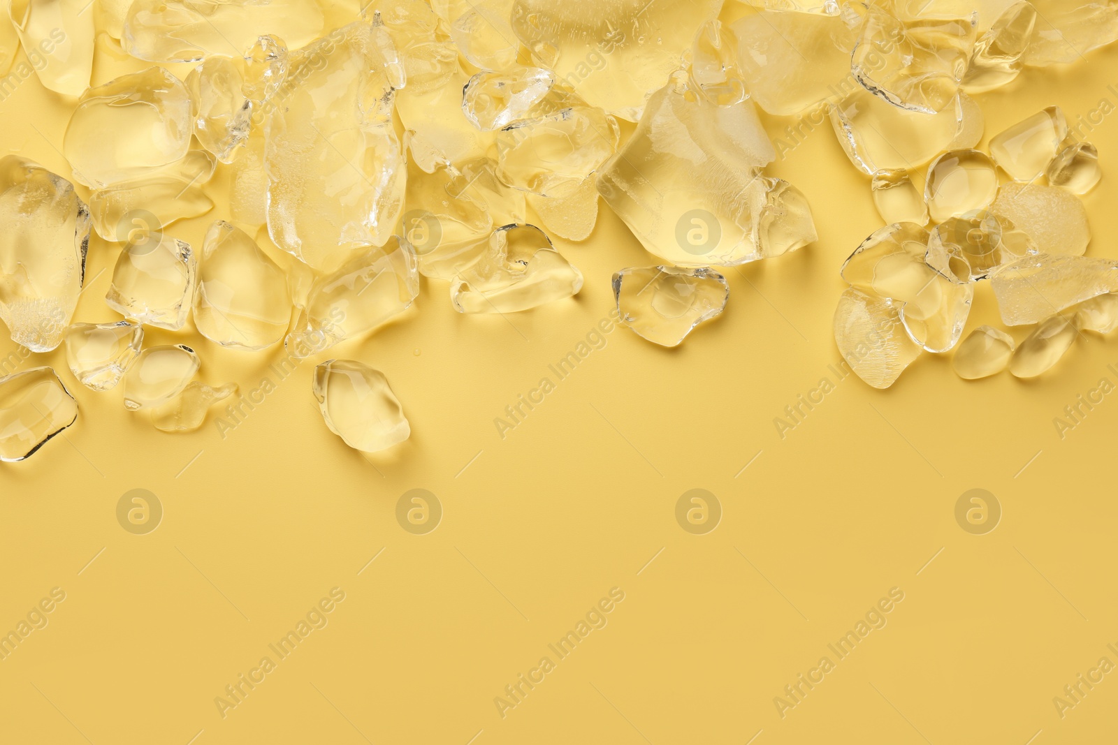 Photo of Pieces of crushed ice on yellow background, top view. Space for text