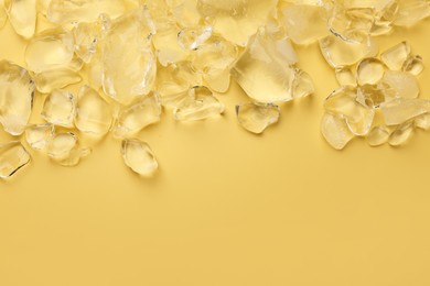 Pieces of crushed ice on yellow background, top view. Space for text