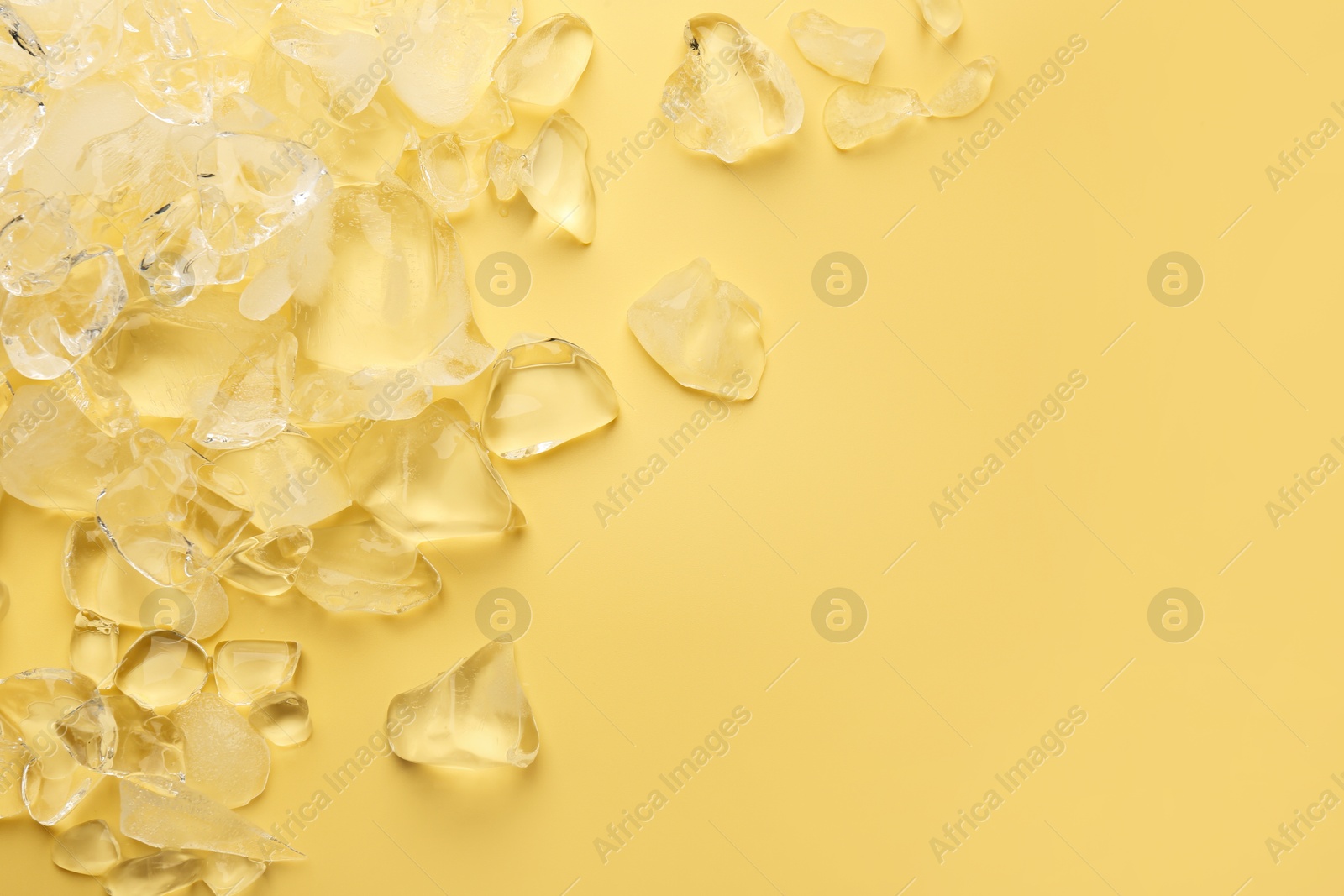 Photo of Pieces of crushed ice on yellow background, top view. Space for text