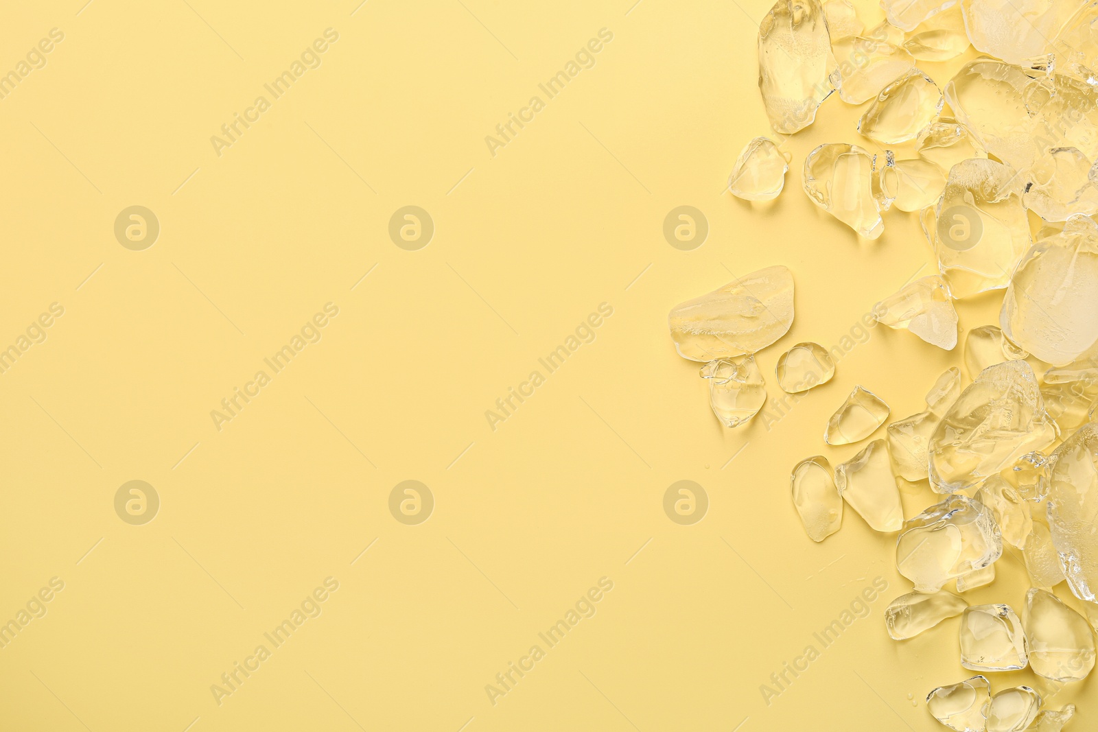 Photo of Pieces of crushed ice on yellow background, top view. Space for text