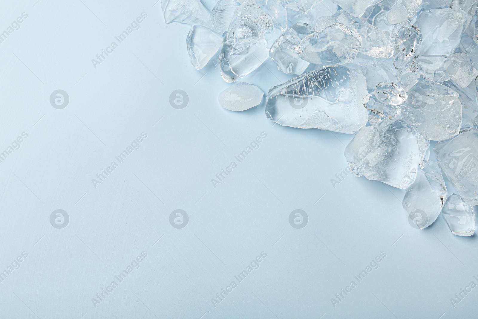 Photo of Pieces of crushed ice on light blue background, top view. Space for text