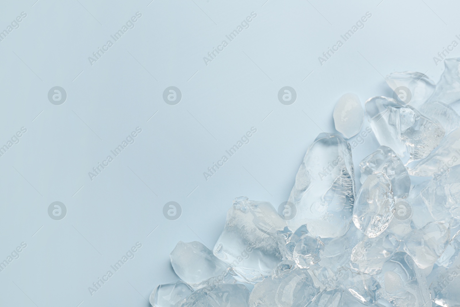 Photo of Pieces of crushed ice on light blue background, top view. Space for text