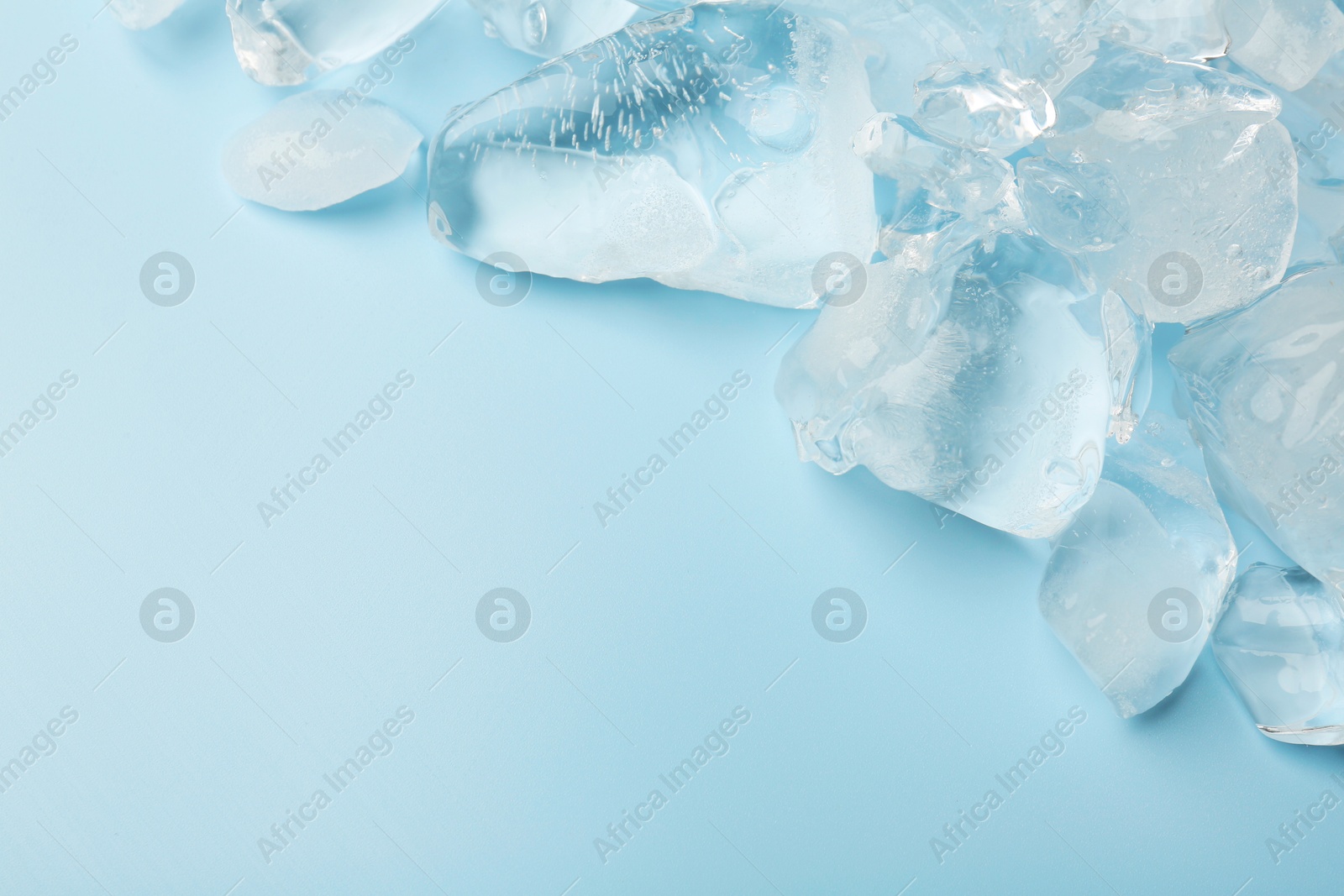 Photo of Pieces of crushed ice on light blue background, space for text