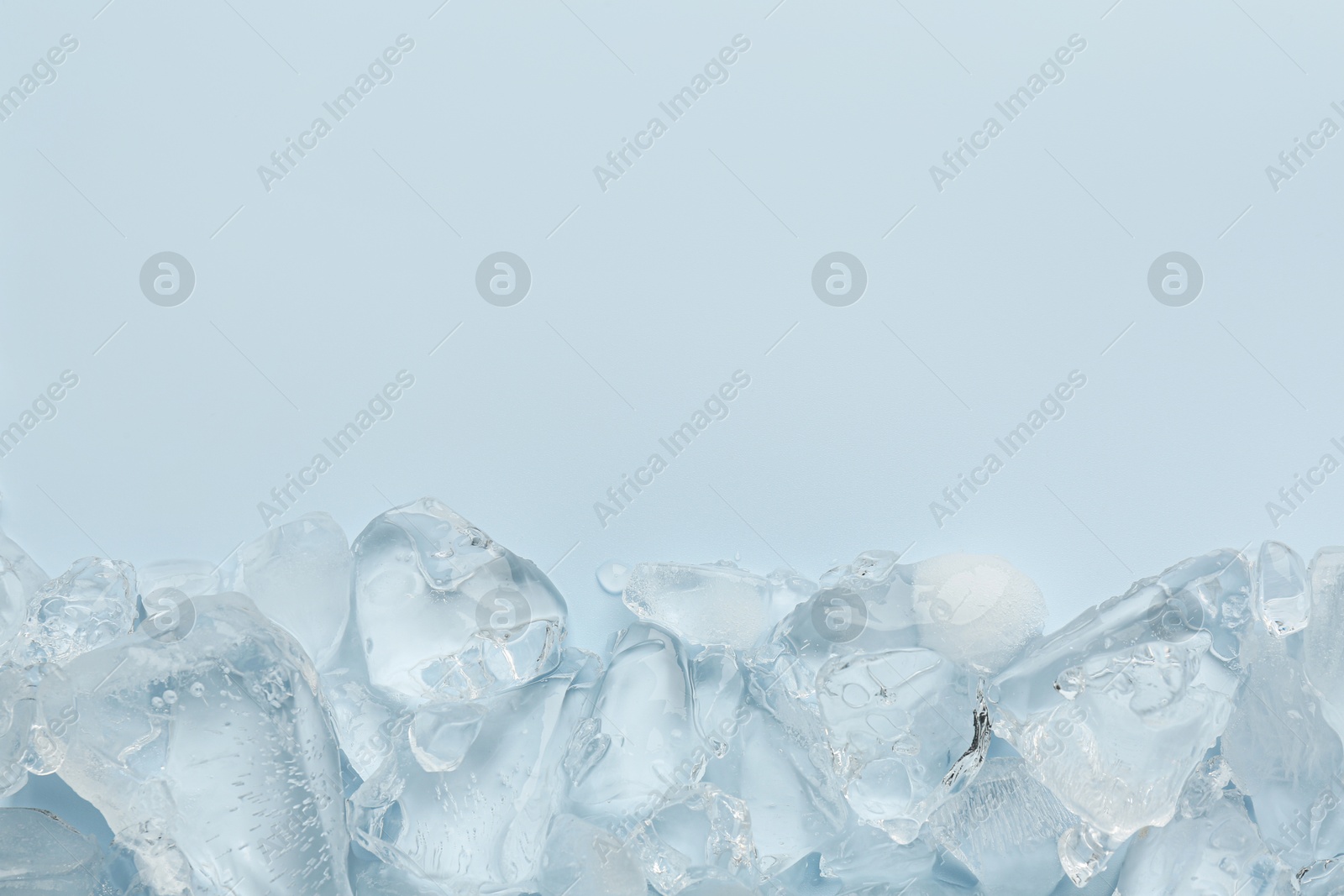 Photo of Pieces of crushed ice on light blue background, top view. Space for text