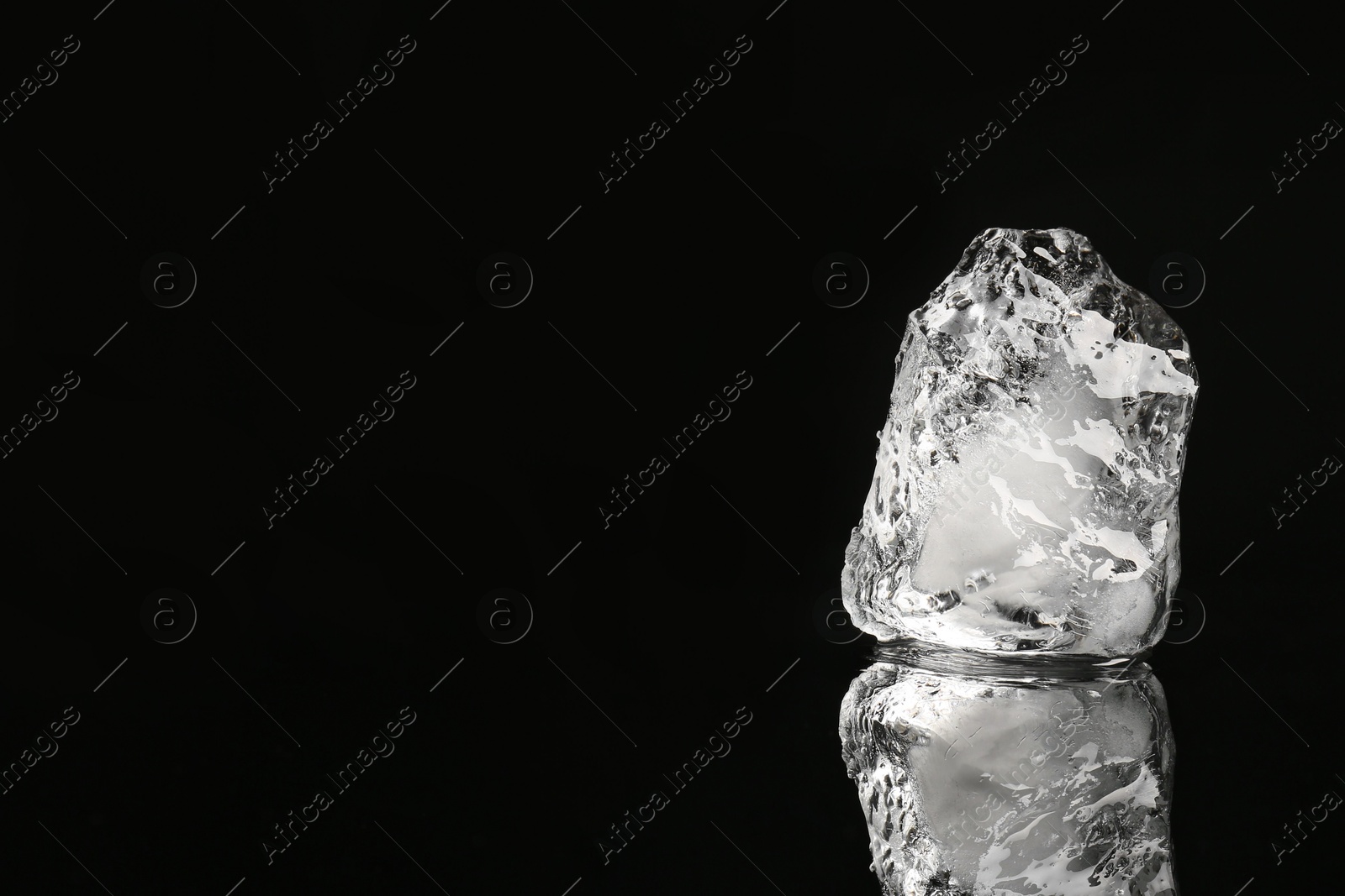 Photo of Piece of clear ice on black mirror surface, space for text