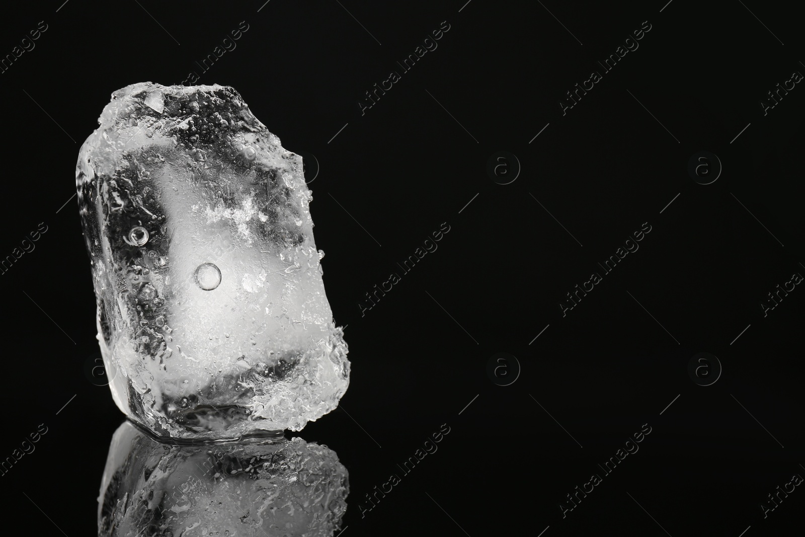 Photo of Piece of clear ice on black mirror surface, space for text