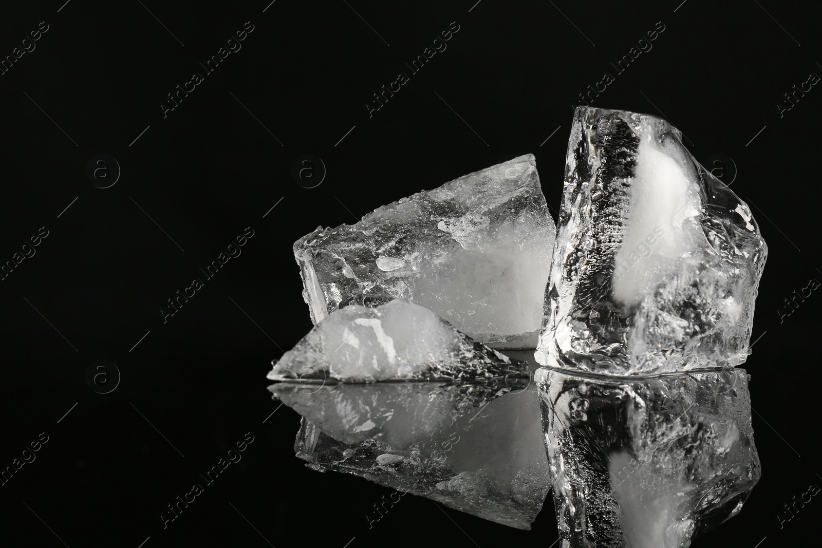 Photo of Pieces of clear ice on black mirror surface, space for text