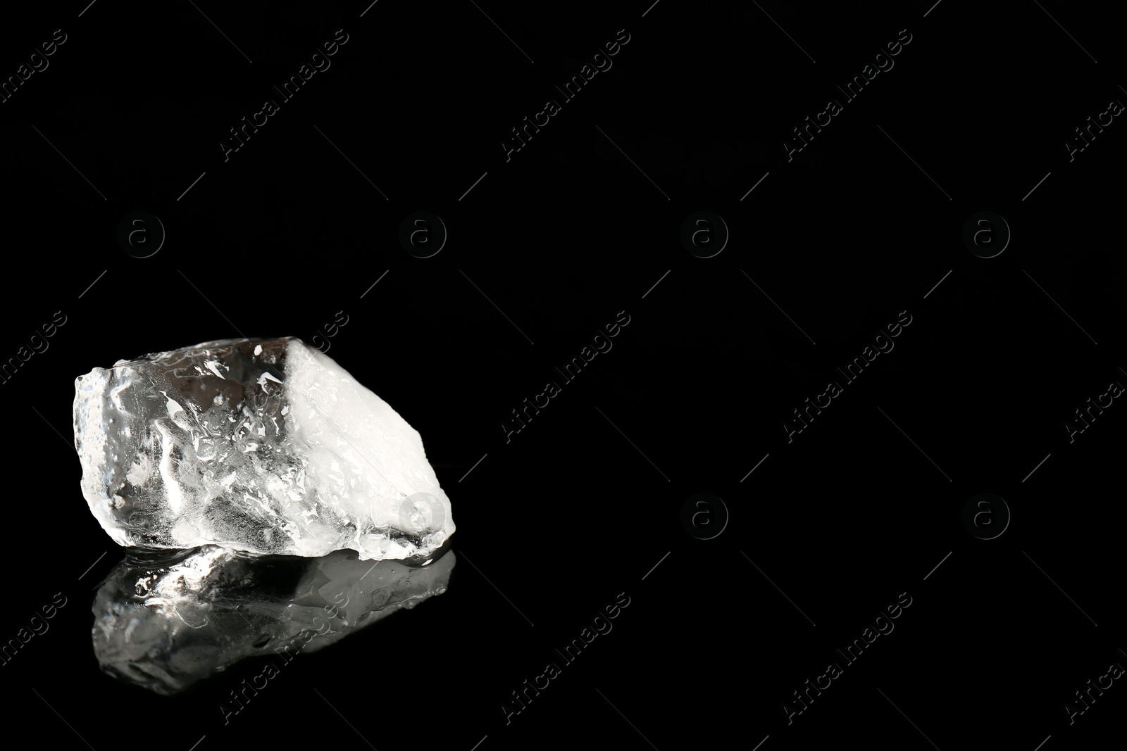 Photo of Piece of clear ice on black mirror surface, space for text