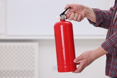 Photo of Man with fire extinguisher indoors, closeup. Space for text