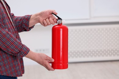 Man with fire extinguisher indoors, closeup. Space for text