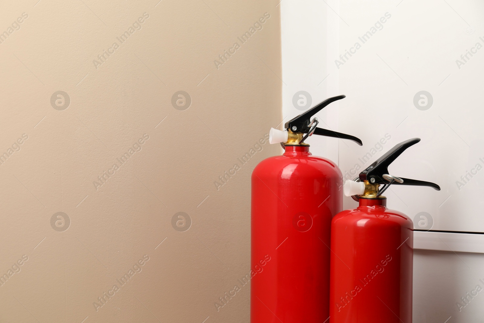 Photo of Two fire extinguishers near beige wall indoors, space for text