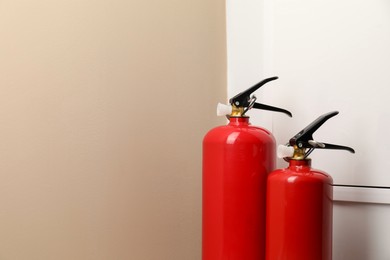 Two fire extinguishers near beige wall indoors, space for text